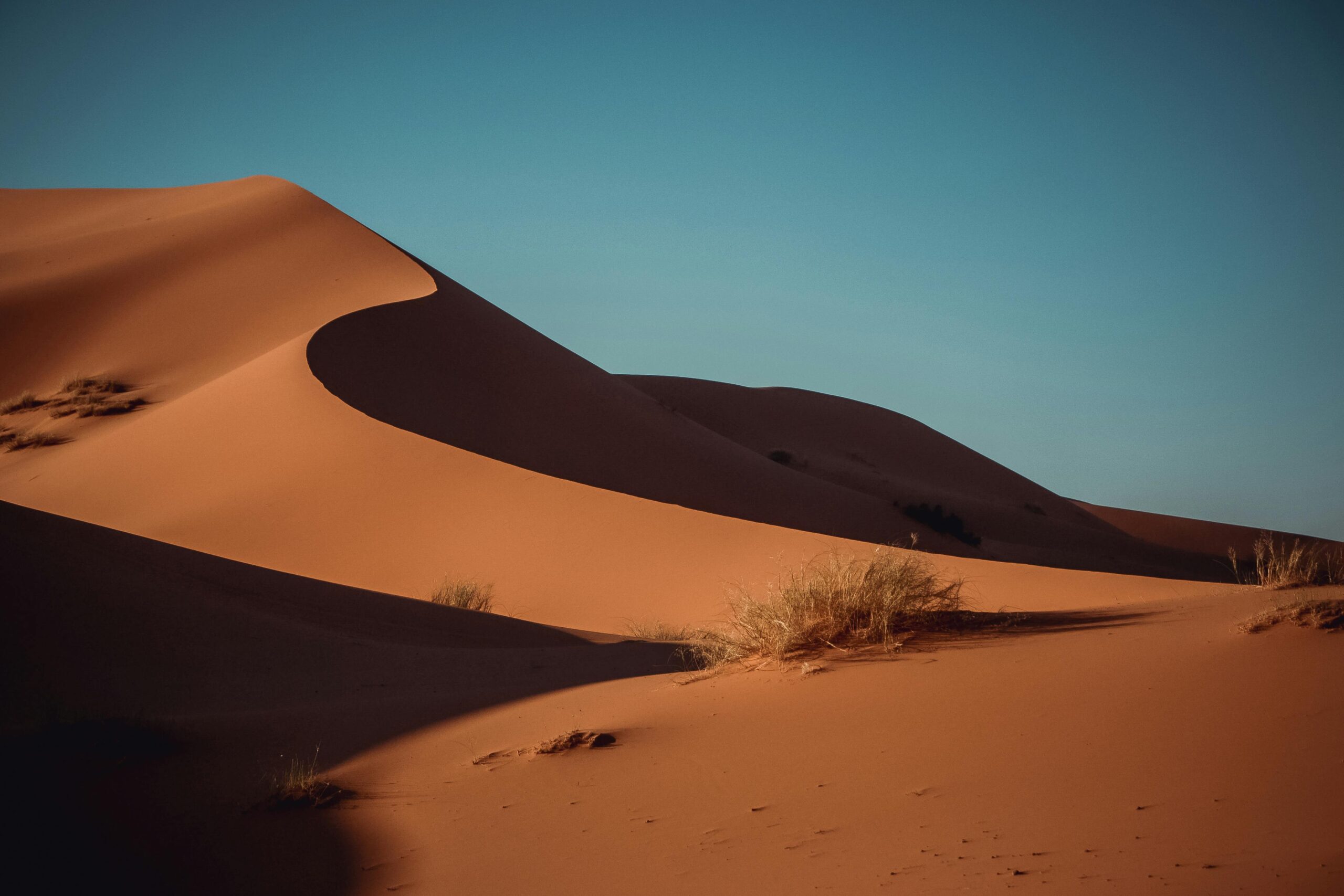 Serene sand dunes in Merzouga glow under a brilliant sunset sky, capturing the essence of the Sahara desert.