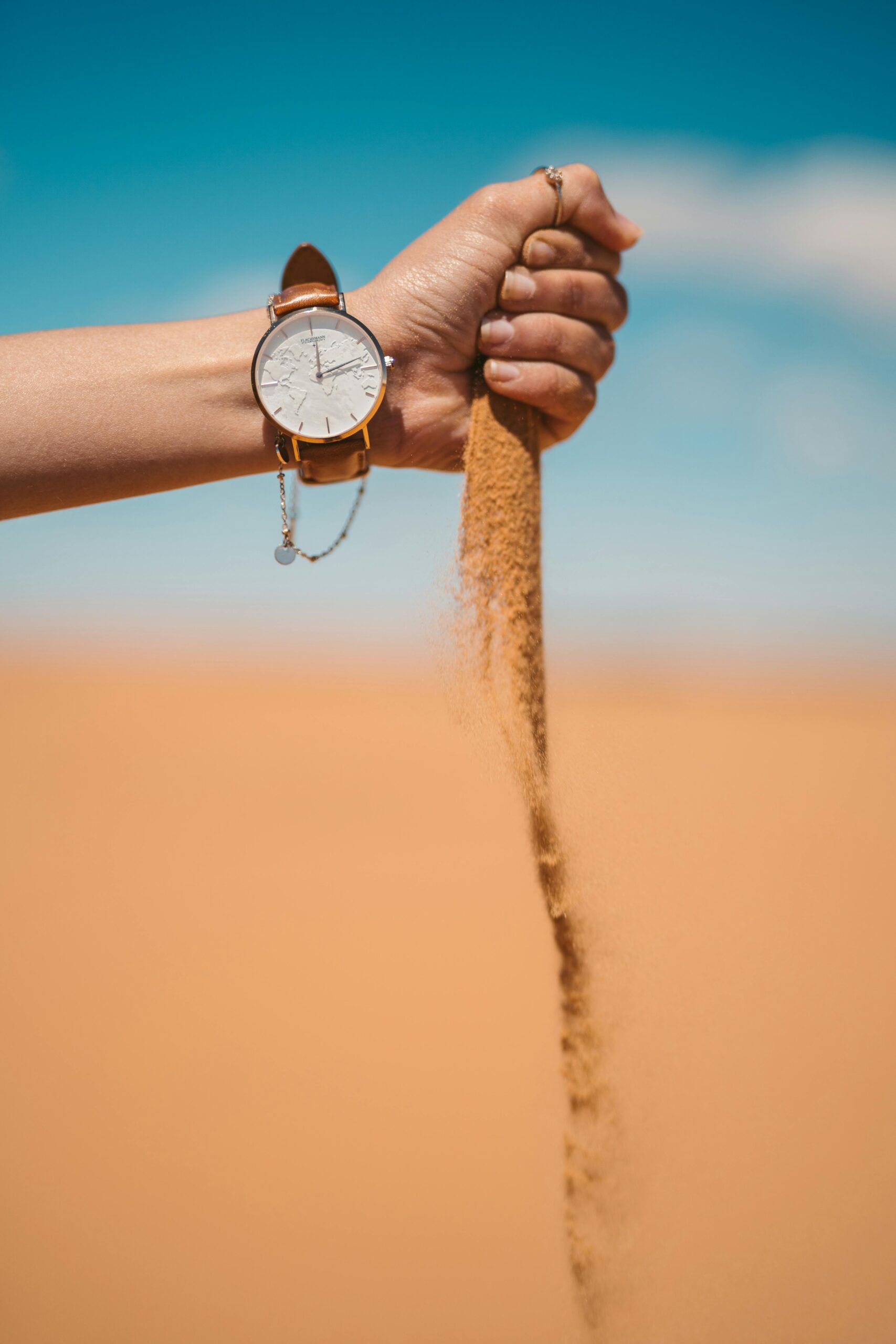 A watch on a hand pouring sand in the Moroccan desert under a clear blue sky.