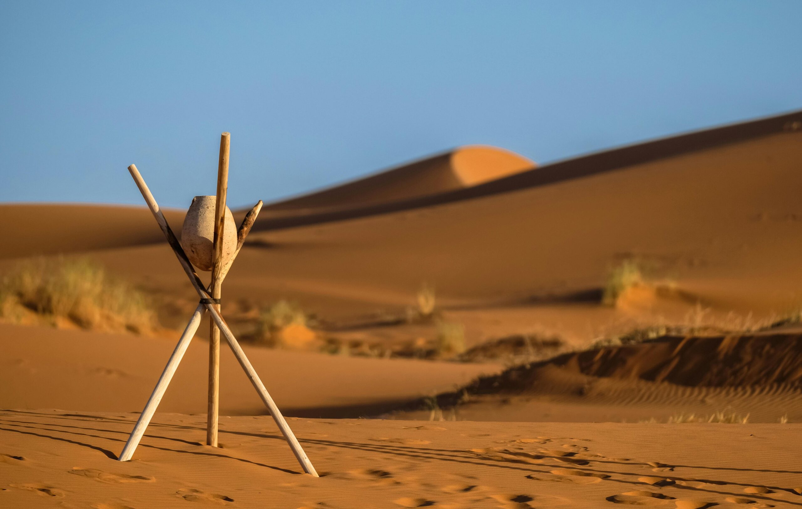 Peaceful desert landscape at Merzouga with sand dunes and wooden tripod under clear blue sky.